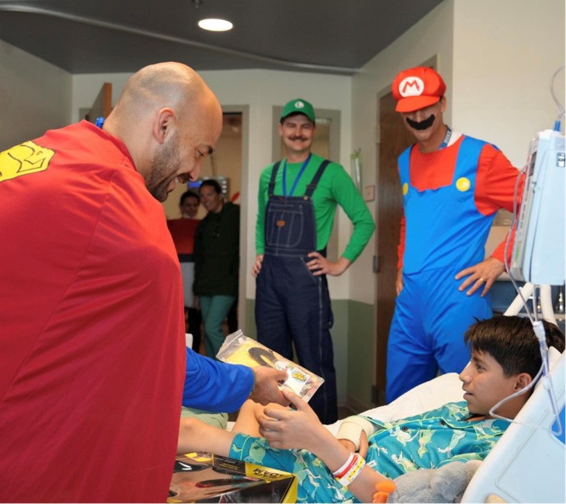 A man dressed as Superman visits with a pediatric patient.